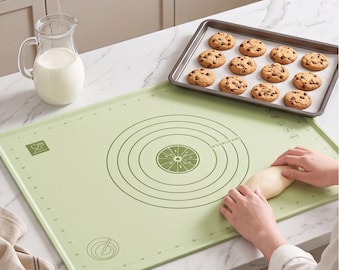 Op de afbeelding: Een rechthoekige lichtgroene siliconen bakmat met donkergroene opgedrukte maataanduidingen, concentrische cirkels en een centrale afbeelding van een citrusvrucht. De mat bevat een klein logo en de tekst SHUANCHANG.