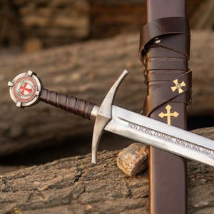 Peut inclure: Une épée en acier avec une poignée gainée de cuir marron et un pommeau circulaire orné d'une croix rouge. La lame porte l'inscription latine NON NOBIS, DOMINE, NON NOBIS, SED NOMINI TUO DA GLORIAM. Elle est accompagnée d'un fourreau en cuir marron.
