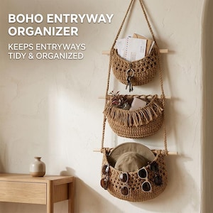 May include: A hanging wall organiser featuring three brown crocheted baskets suspended by rope and wooden dowels. The text BOHO ENTRYWAY ORGANIZER KEEPS ENTRYWAYS TIDY & ORGANIZED is visible. The baskets hold envelopes, keys, a hat, and sunglasses.
