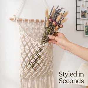 May include: A cream-coloured macrame wall hanging featuring a diamond-patterned net design suspended from a wooden dowel with a rope hanger. The pocket holds a bouquet of dried lavender and tan bunny tail grass. Text reads: Styled in Seconds.