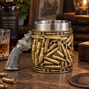 Puede incluir: Una taza cilíndrica con un exterior texturizado cubierto por un patrón en relieve de casquillos de bala dorados. El asa tiene la forma de la empuñadura de un revólver plateado. El interior de la taza está revestido de acero inoxidable pulido.