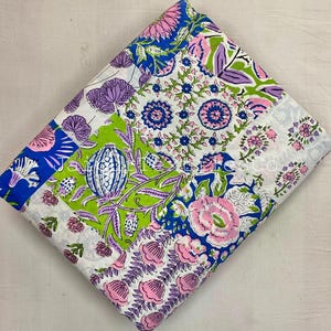 May include: A folded piece of fabric featuring a vibrant floral pattern with shades of pink, purple, bright green, and blue on a white background. The design includes various botanical motifs, including large blossoms, small clusters of flowers, and leafy vines arranged in a dense, repeating layout across the textile surface.
