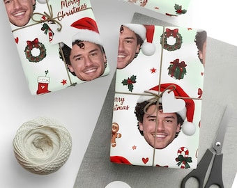 Può includere: Carta da regalo personalizzata con un motivo ripetuto di una persona sorridente con cappello da Babbo Natale, intervallato da illustrazioni di ghirlande natalizie, calze, bastoncini di zucchero, omini di pan di zenzero e la scritta Merry Christmas.