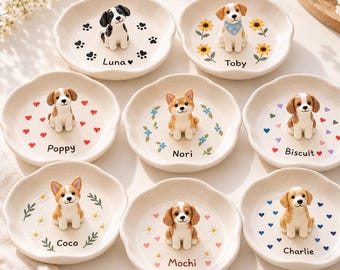May include: Eight small, round, off-white ceramic trinket dishes with scalloped edges. Each dish features a unique 3D dog figurine in the center and is personalized with a name: Luna, Toby, Poppy, Nori, Biscuit, Coco, Mochi, and Charlie.