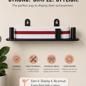 Op de afbeelding: Een zwarte wandplank voor vechtsportriemen met de tekst STRONG. SIMPLE. STYLISH. De plank bevat een witte riem met een rode streep. Daaronder staan iconen en tekst: DURABLE, EASY TO INSTALL, HOLDS ALL BELTS, SLEEK DESIGN en Earn it. Display it. Be proud. Every belt tells a story.