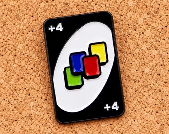Puede incluir: Un pin de esmalte rectangular con forma de carta de juego con fondo negro y un óvalo blanco en el centro. La carta presenta el texto +4 en las esquinas superior izquierda e inferior derecha, con un grupo de pequeños rectángulos rojos, azules, amarillos y verdes.