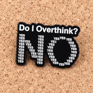 May include: A black enamel pin with white text that reads Do I Overthink? at the top. Below the question, the word NO is formed by repeating the word YES in white text multiple times, creating a large, bold typographic design on the pin surface.