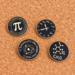 May include: Four round black enamel pins with gold-tone metal edges. One features the pi symbol and digits, one a clock with chemical element symbols, one an atom graphic with the text Science, it's like magic but real, and one a caffeine molecule.