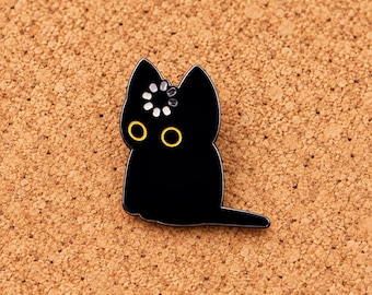 Puede incluir: Un pin de esmalte negro con forma de gato sentado, con un icono de carga blanco en la frente y dos ojos delineados en amarillo. El gato tiene orejas puntiagudas y una cola que se extiende hacia la derecha, con un acabado liso y brillante.