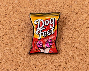 Puede incluir: Un pin de esmalte metálico con forma de bolsa de snacks con la parte superior amarilla y la inferior roja. El texto "Dog Feet" está impreso en blanco, con la palabra "ORIGINAL" debajo. El diseño muestra dos patas de animal marrones y blancas.
