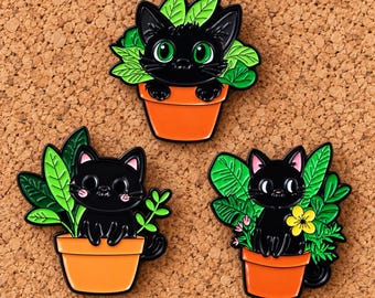 Puede incluir: Tres pines de esmalte con gatos negros sentados en macetas de terracota naranja rodeados de follaje verde. El pin superior muestra un gato con grandes ojos verdes, mientras que los dos inferiores tienen orejas con detalles en color rosa.