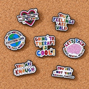 Peut inclure: Un ensemble de sept épinglettes en émail colorées avec des affirmations sur la santé mentale. Les motifs incluent un cœur arc-en-ciel, un globe, un cerveau et des textes comme You Are More Loved Than You Know, Your Feelings Are Valid, Going To Therapy Is Cool, Let's Talk About Mental Health, You Are Enough et You Are Not Your Anxious Thoughts.