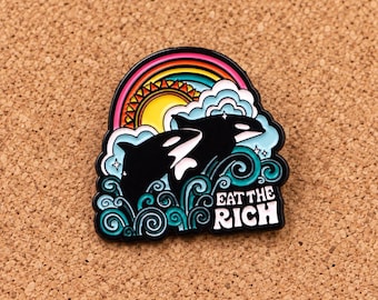 Puede incluir: Un pin de esmalte en blanco y negro que muestra dos orcas saltando a través de olas turquesas bajo un sol amarillo y un arcoíris colorido. El diseño incluye nubes blancas y el texto EAT THE RICH en letras mayúsculas blancas en la parte inferior.
