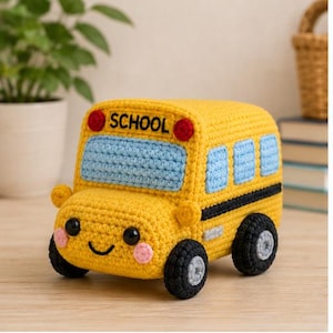 May include: A yellow crocheted school bus toy with a smiling face, black wheels, and light blue windows. The front features the word SCHOOL in black letters, two red circular lights, and pink cheeks. The bus has a textured yarn construction.