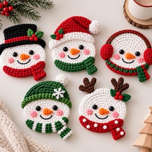Könnte beinhalten: Fünf runde Häkeluntersetzer in Form von Schneemann-Gesichtern. Jeder hat schwarze Perlenaugen, eine orangefarbene Karottennase und rosa Wangen. Sie tragen verschiedene Winteraccessoires, darunter einen schwarzen Zylinder, eine rote Weihnachtsmannmütze, rote Ohrenschützer, eine grüne Mütze und ein braunes Rentiergeweih mit roten Stechpalmenbeeren.