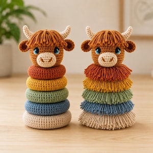 May include: Two crochet highland cow stacking toys. The left toy features smooth, solid-colored rings in rust, yellow, sage green, blue, and beige. The right toy features textured, fringed rings in matching colors. Both have brown heads with bangs.