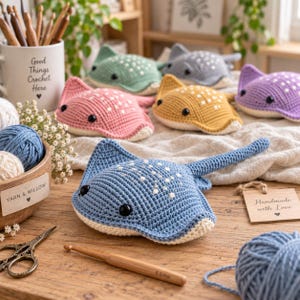 May include: A collection of handmade crochet stingray plushies in various colors including blue, pink, yellow, green, and purple. Each stingray features black safety eyes and white embroidered spots on the top surface, with a cream-colored underside.