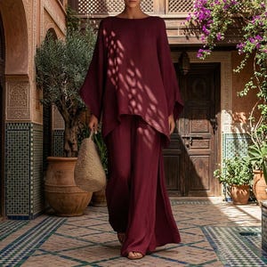 Peut inclure: Un ensemble deux pièces bordeaux profond composé d'un haut ample à manches longues avec une large encolure arrondie et d'un pantalon assorti à jambes larges. La tenue est en tissu uni et accompagnée d'un sac à main tissé beige clair texturé.