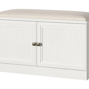 May include: A white wooden storage bench featuring two cabinet doors with recessed panels and small round bronze-toned knobs. The top of the bench is fitted with a rectangular, light beige upholstered cushion that spans the entire length.
