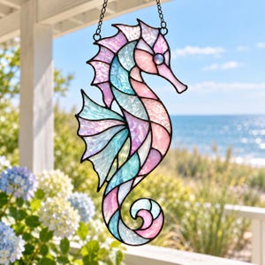 May include: A stained glass seahorse suncatcher featuring iridescent panels in shades of pastel pink, light blue, and white. The seahorse is constructed with dark metal solder lines and includes a metal chain at the top for hanging purposes.