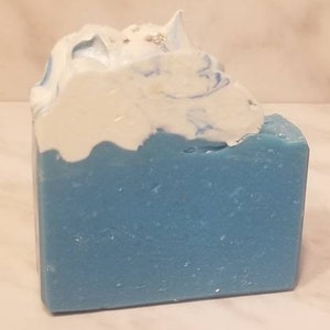 Puede incluir: Una pastilla de jabón azul y blanco con la parte superior blanca y la inferior azul. El jabón tiene un patrón de remolino y está hecho con ingredientes naturales.