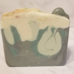 Könnte beinhalten: Eine handgemachte Seife in Form eines Blocks mit einem Wirbelmuster in Grün-, Weiß- und Grautönen.