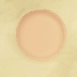 Puede incluir: Una bandeja redonda de cer&aacute;mica de color rosa p&aacute;lido con un borde festoneado. La bandeja es lisa.
