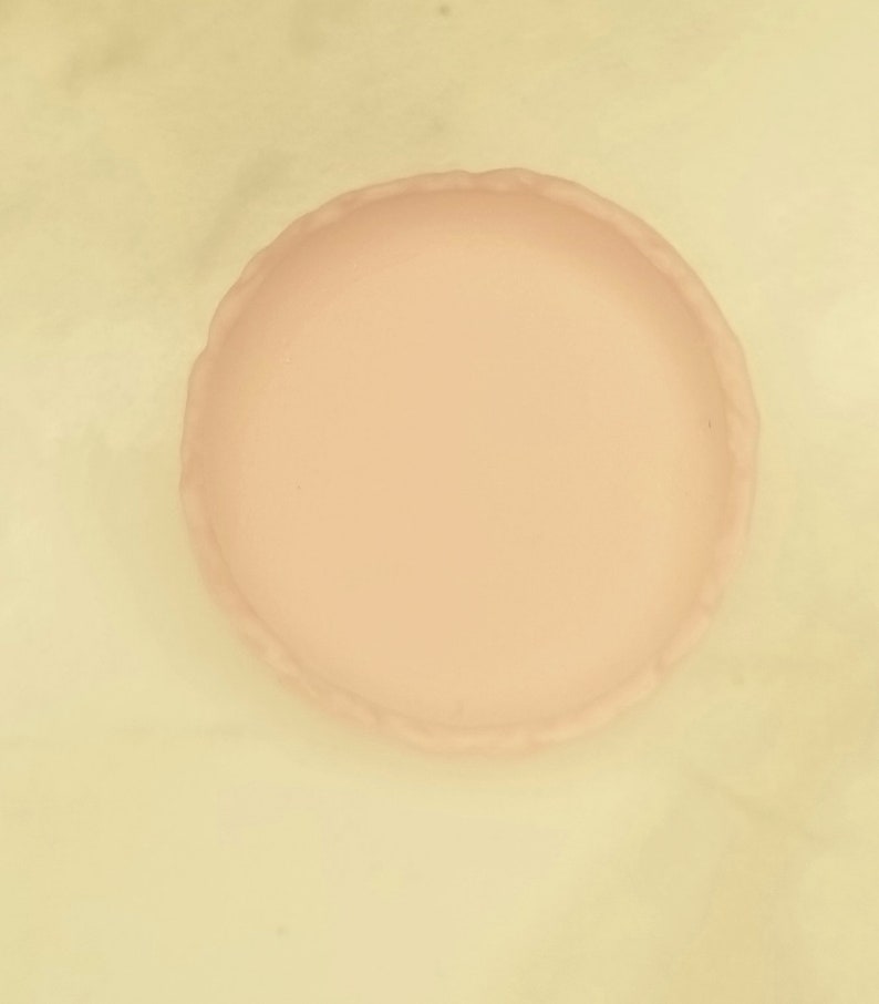 Puede incluir: Una bandeja redonda de cer&aacute;mica de color rosa p&aacute;lido con un borde festoneado. La bandeja es lisa.