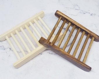 Könnte beinhalten: Zwei Seifenablagen aus Holz, eine naturbelassen und eine braun gebeizt. Beide haben ein Lamellendesign, damit die Seife abtropfen kann.
