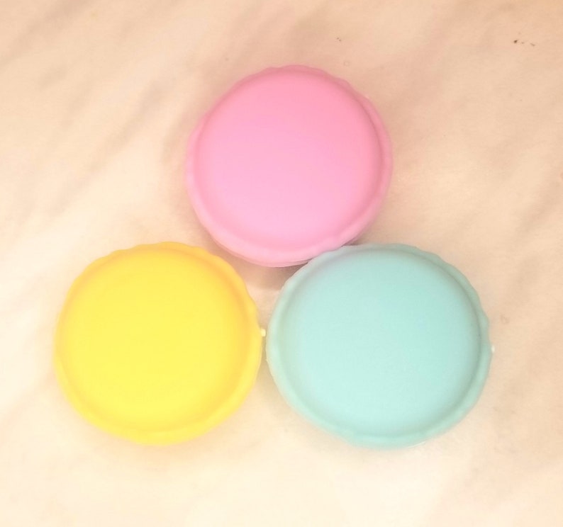 Puede incluir: Tres macarons redondos y coloridos. Uno es rosa, otro amarillo y otro azul claro.
