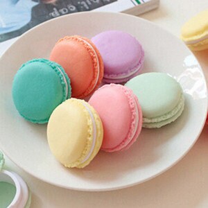 Puede incluir: Seis recipientes en forma de macaron de color pastel con tapas blancas. Los recipientes est&aacute;n dispuestos en c&iacute;rculo sobre un plato blanco.