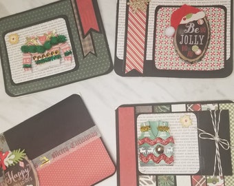 Puede incluir: Cuatro tarjetas de Navidad hechas a mano con diferentes diseños. Las tarjetas presentan una cinta de cuadros verde y roja, una cinta a rayas roja y blanca, un papel estampado verde y blanco y un papel estampado negro y blanco. Las tarjetas también presentan una variedad de adornos, incluyendo un letrero de madera que dice "Be Jolly", un pequeño árbol de Navidad y un pequeño muñeco de nieve.
