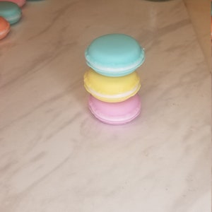 Puede incluir: Una pila de tres macarons de color pastel. El macaron de arriba es azul claro, el macaron del medio es amarillo y el macaron de abajo es rosa.