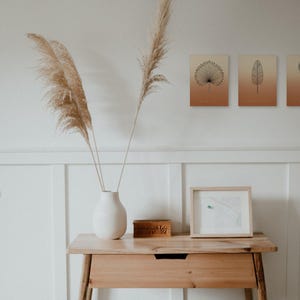 May include: Three rectangular wall art prints featuring black botanical line drawings of a palm leaf, a banana leaf, and a protea flower against a gradient background transitioning from cream to terracotta orange.