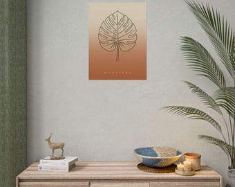 May include: A rectangular wall art print featuring a black line drawing of a monstera leaf centered on a gradient background that transitions from light beige at the top to a warm terracotta orange at the bottom, with the text MONSTERA printed below.
