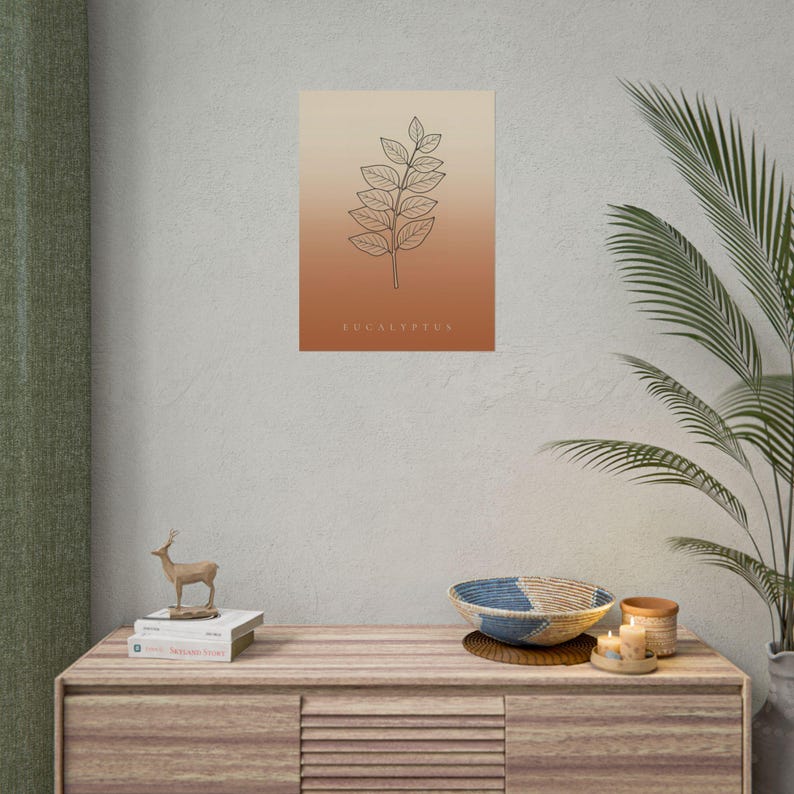 May include: A rectangular wall art print featuring a black line drawing of a eucalyptus branch centered on a vertical gradient background that transitions from light beige at the top to a deep terracotta orange at the bottom with the word EUCALYPTUS.