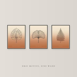 May include: Three framed wall art prints featuring black line drawings of a monstera leaf, a ginkgo leaf, and a fern leaf. Each print has a gradient background transitioning from light beige to terracotta orange. The text DREI MOTIVE, EINE WAND is below.