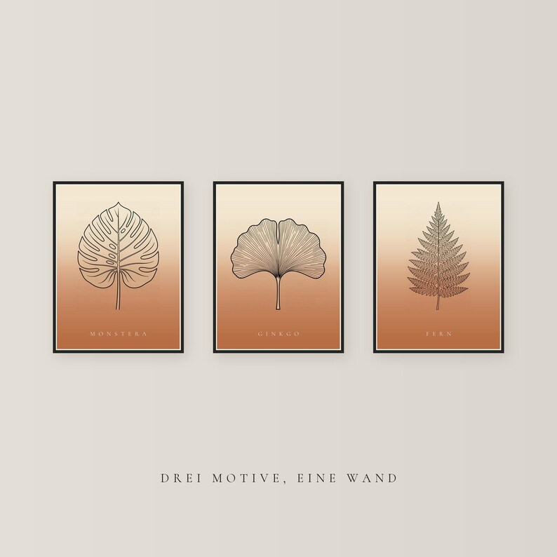 May include: Three framed wall art prints featuring black line drawings of a monstera leaf, a ginkgo leaf, and a fern leaf. Each print has a gradient background transitioning from light beige to terracotta orange. The text DREI MOTIVE, EINE WAND is below.