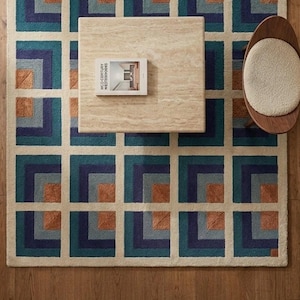 Può includere: Un tappeto rettangolare caratterizzato da un motivo geometrico ripetitivo di quadrati annidati in tonalità verde acqua, blu navy e arancione bruciato, separati da bordi color crema. Il tappeto è posizionato sotto un tavolino quadrato in travertino.