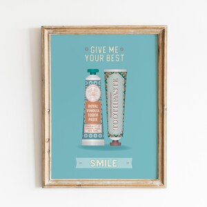 May include: A framed print with a blue background featuring two tubes of toothpaste. The text on the print reads "Give me your best" and "Smile".