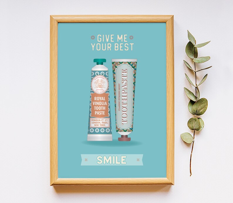 May include: A framed print with a light blue background featuring two vintage-style toothpaste tubes. The text on the print reads "Give me your best" and "Smile".