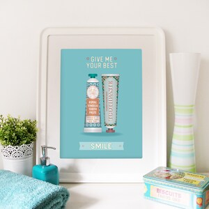 May include: A turquoise blue framed print with the text "Give me your best" and "Smile" in white. The print features two vintage-style toothpaste tubes with a teal and gold design.
