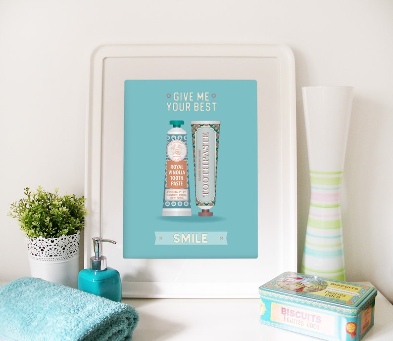 May include: A turquoise blue framed print with the text "Give me your best" and "Smile" in white. The print features two vintage-style toothpaste tubes with a teal and gold design.