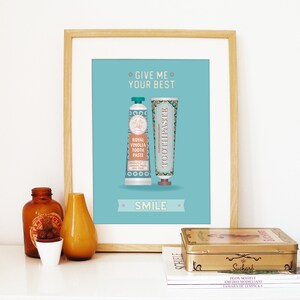 May include: A framed print with a light blue background featuring two vintage toothpaste tubes with the text "Give me your best" and "Smile".