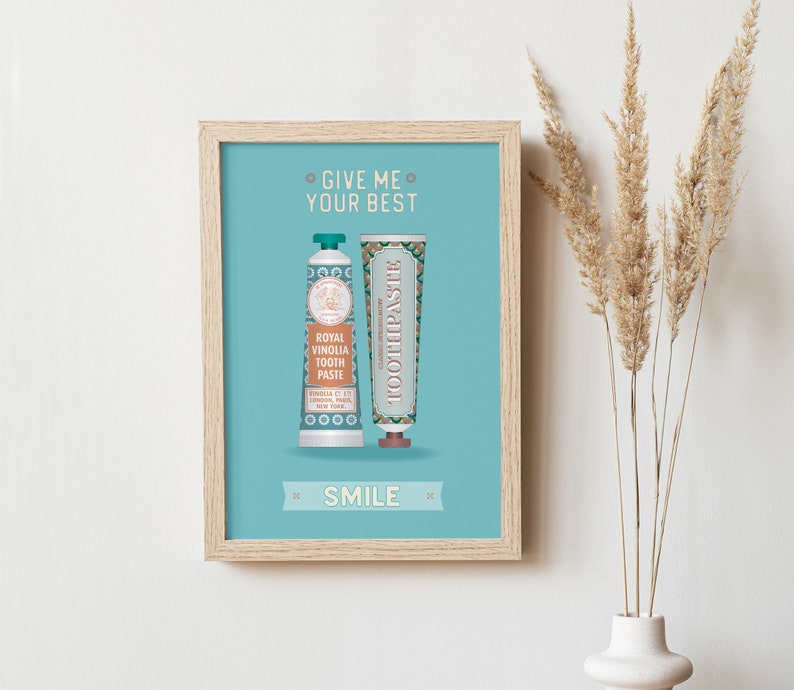 May include: A light blue framed print with the text "Give me your best" and "Smile" in a white font. The print features two tubes of toothpaste, one with a green and gold design and the text "Royal Vinolia Tooth Paste" and the other with a blue and gold design and the text "Toothpaste".
