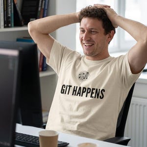 May include: A cream-colored short-sleeve t-shirt featuring a black graphic of a tangled ball of yarn above the bold black text that reads GIT HAPPENS. The shirt has a crew neckline and a standard fit, made of a solid light-colored fabric.