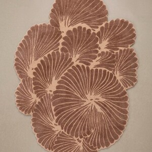 May include: A tufted rug featuring an organic, irregular shape composed of multiple overlapping fan-like motifs. The design displays a two-tone color palette of deep brown and light beige, with the darker brown fibers forming the raised, textured radial patterns.