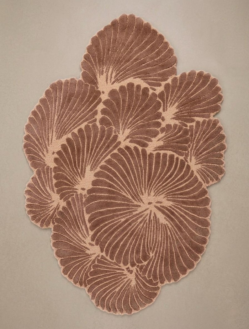May include: A tufted rug featuring an organic, irregular shape composed of multiple overlapping fan-like motifs. The design displays a two-tone color palette of deep brown and light beige, with the darker brown fibers forming the raised, textured radial patterns.