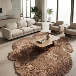 May include: A large, irregularly shaped area rug in a warm beige tone, featuring a repeating pattern of raised, fan-like petal motifs that create a textured, organic surface. The rug is positioned on a smooth floor beneath a wooden coffee table.