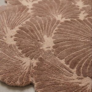 May include: A tufted area rug in a dusty rose color featuring a repeating pattern of fan-shaped or shell-like motifs. The design consists of raised, textured lines radiating from a central point within each shape, creating a soft, plush surface.